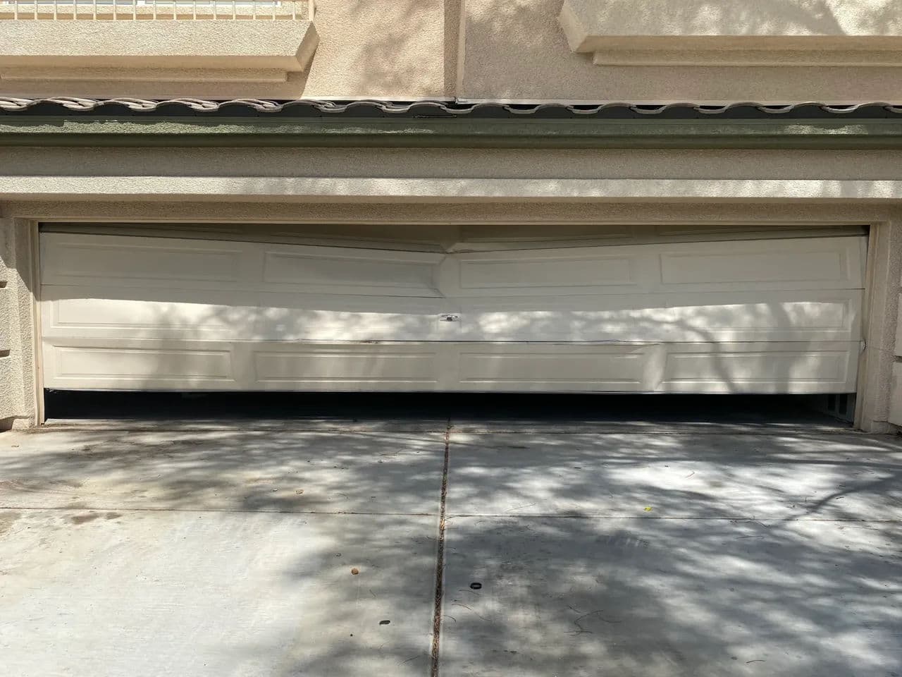 Damaged garage door with visible dents and warping, set against a residential backdrop.
